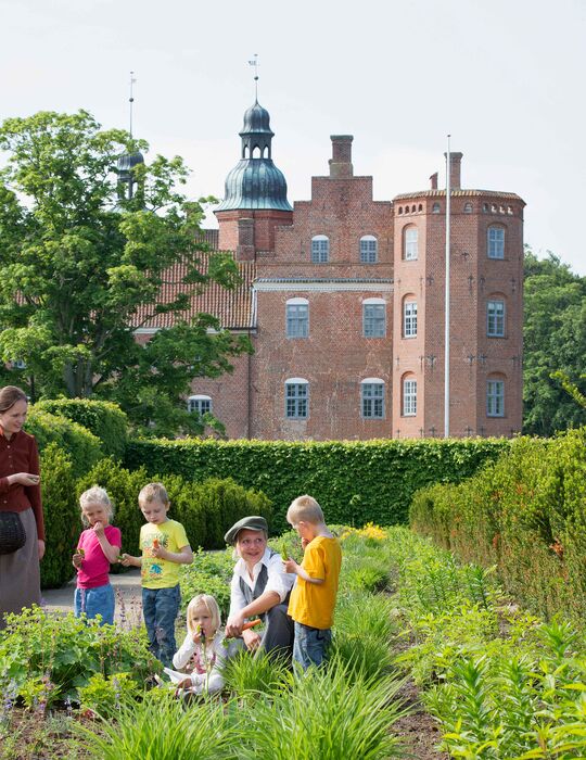En gruppe børn og formidlere i dragt i herregårdshaven på Gammel Estrup en sommerdag 